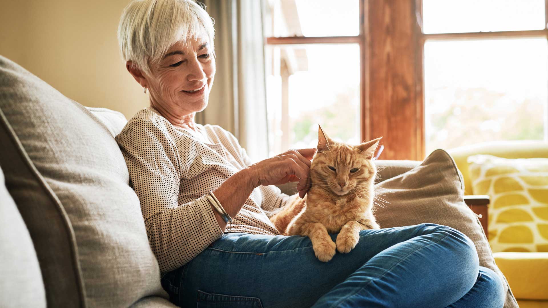 An older woman on the couch with her orange cat