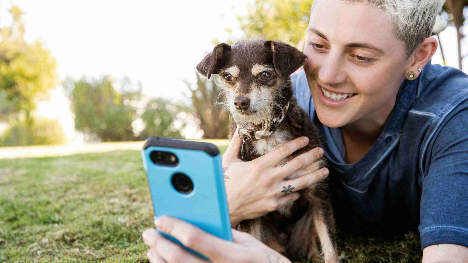A woman in a field with their dog looking at their phone