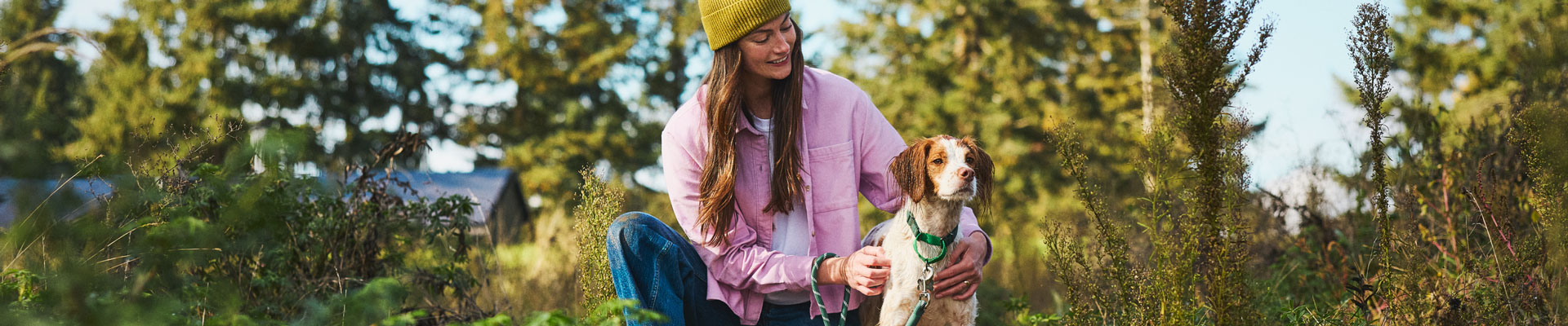 A woman in a green beanie walking her Brittany Spaniel through a foresty area