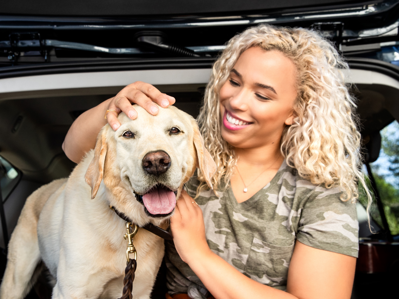 A dog owner sitting with her dog in the back of her car and fondly petting her dog