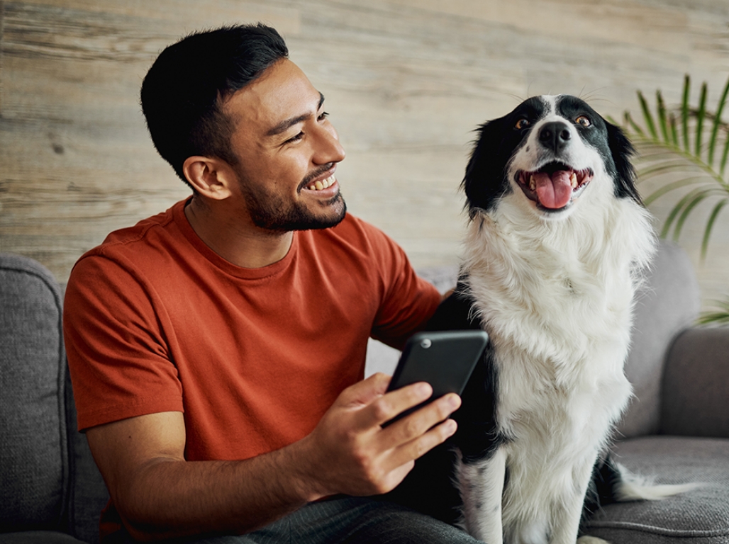 A man scrolls his mobile device next to his black and white dog 