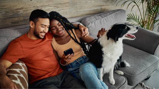 A man and a woman sit on their couch next to their black and white dog