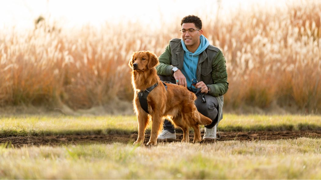A man sits next to his golden retriever outside in a field